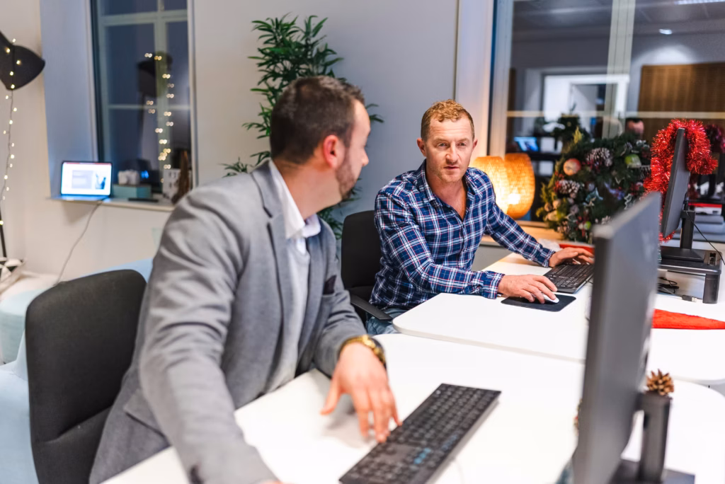 Two brokers working together at a shared office desk with computers