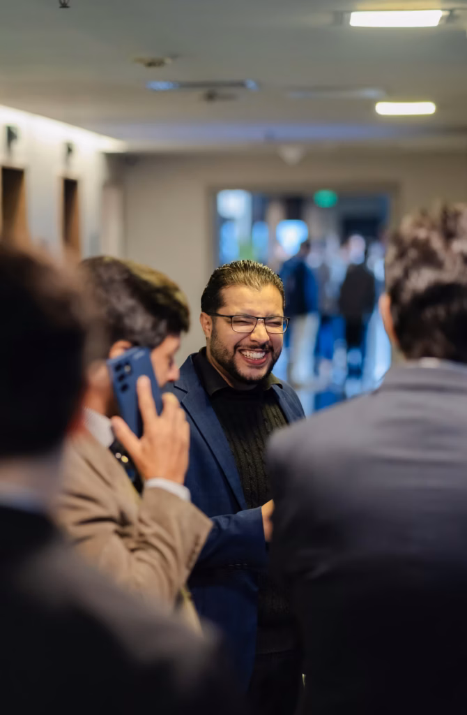 A broker in glasses smiling while talking with colleagues at an industry event